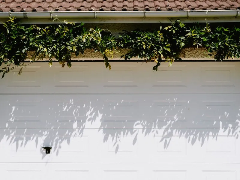 White sectional garage door under tile roof eaves, ready for cable and roller service